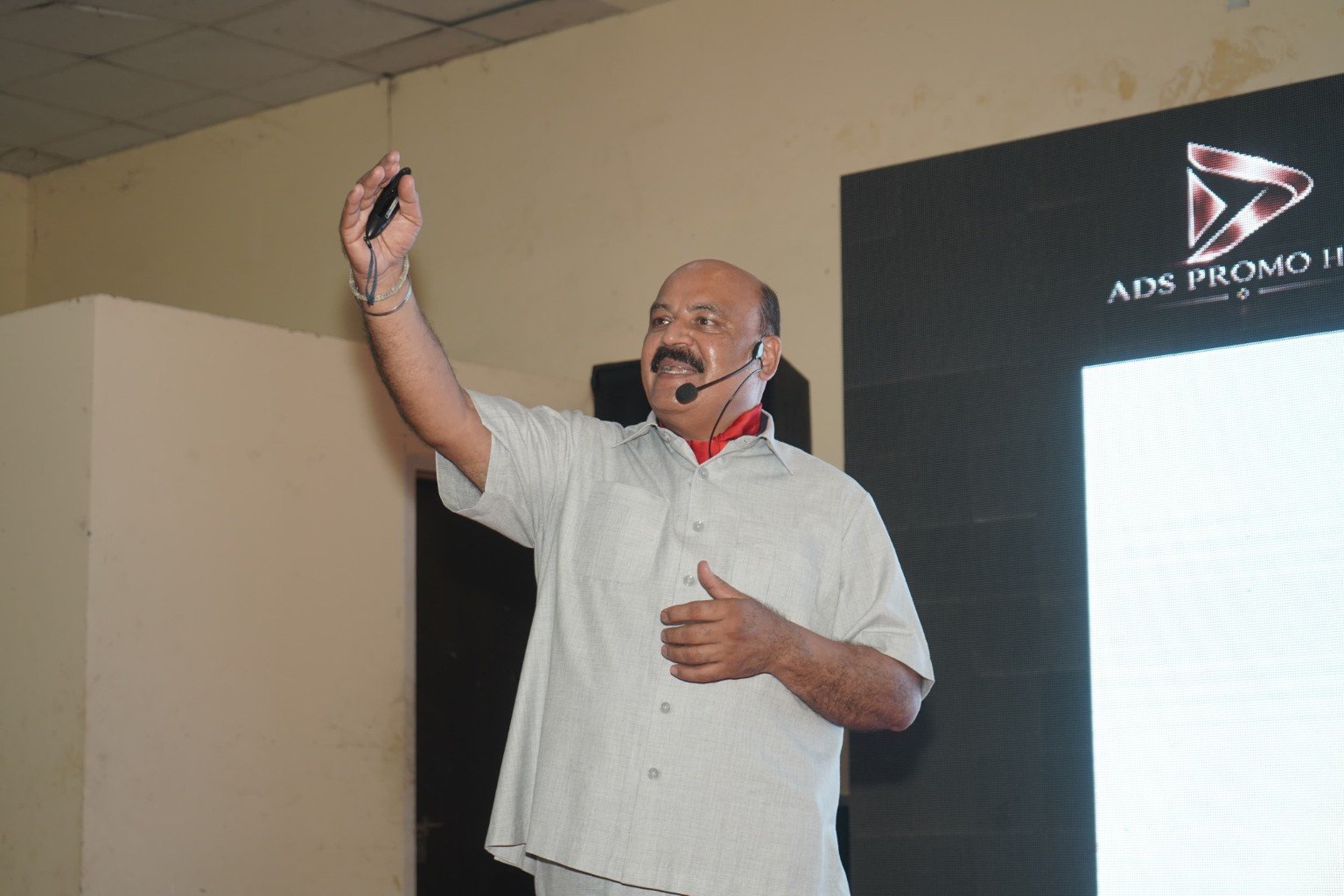 Dr Harish Kant Walia speaking on stage with a headset microphone and raised hand